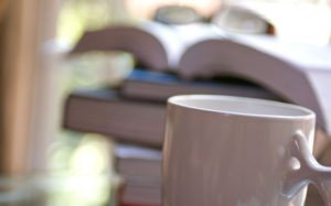 white-ceramic-coffee-cup-in-the-foreground-which-was-placed-in-front-of-a-stack-of-books-725x451